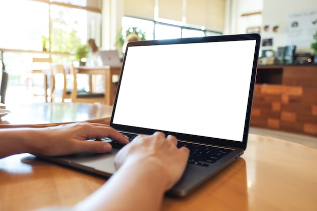 Imagem de maquete de uma mulher usando e digitando no teclado do computador portátil com tela branca em branco na mesa de madeira