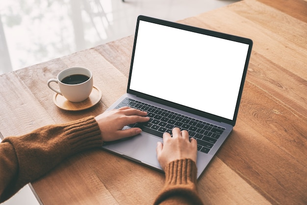 Imagem de maquete de uma mulher usando e digitando no teclado do laptop com a tela do desktop em branco e uma xícara de café na mesa de madeira