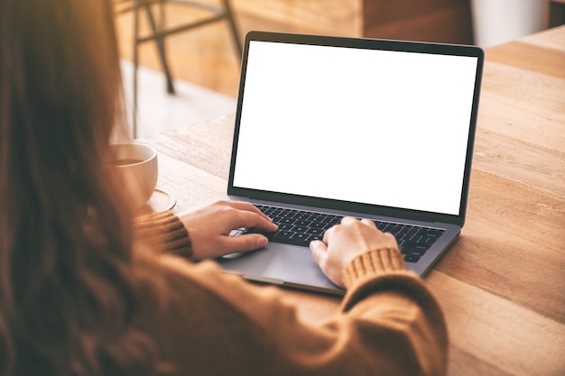 Imagem de maquete de uma mulher usando e digitando no teclado do laptop com a tela do desktop em branco e uma xícara de café na mesa de madeira