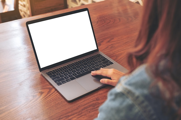 Imagem de maquete de uma mulher usando e tocando no touchpad de laptop com tela de desktop branca em branco em mesa de madeira