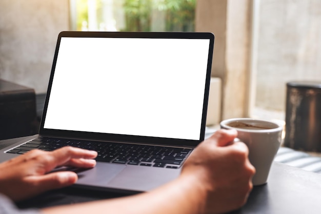 Imagem de maquete de uma mulher usando e tocando no touchpad do laptop com tela branca em branco do desktop enquanto bebe café