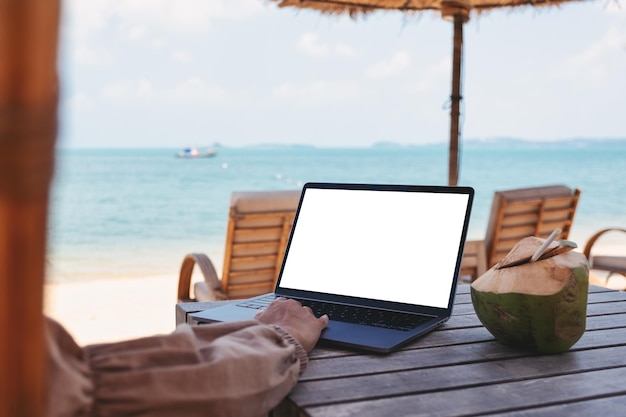 Imagem de maquete de uma mulher usando e tocando no touchpad do laptop com tela em branco do desktop enquanto está sentado na praia