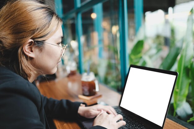 Foto imagem de maquete de uma mulher usando um laptop com tela branca em branco em uma mesa de madeira em um café loft moderno