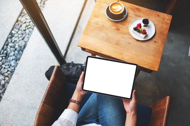 Imagem de maquete de vista superior de uma mulher de negócios segurando um tablet pc preto com uma tela de desktop em branco em um café