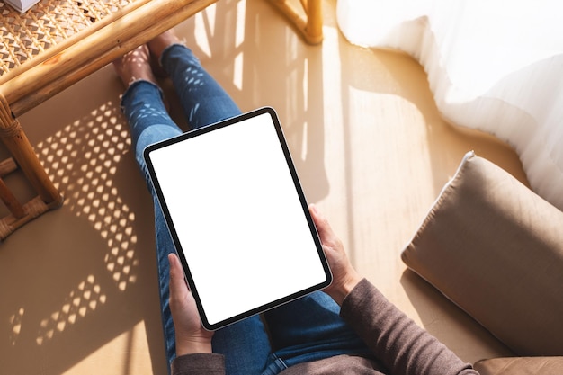 Imagem de maquete de vista superior de uma mulher segurando e usando o tablet pc com tela branca da área de trabalho em branco em casa