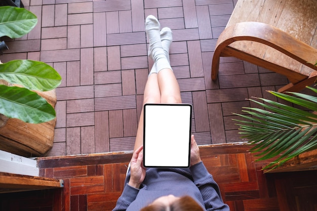 Imagem de maquete de vista superior de uma mulher segurando e usando tablet digital com tela branca em branco do desktop em casa