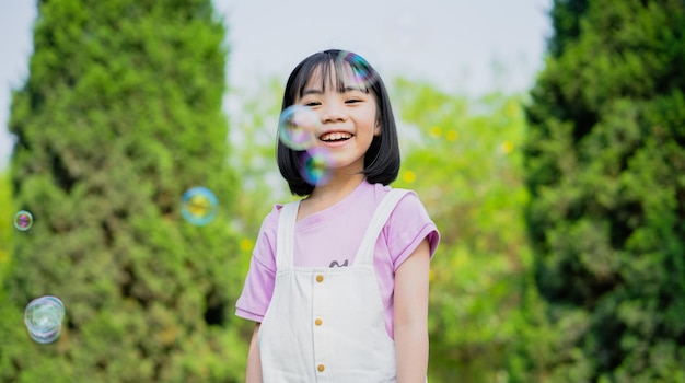 Imagem de menina asiática brincando com bolhas de sabão no parque