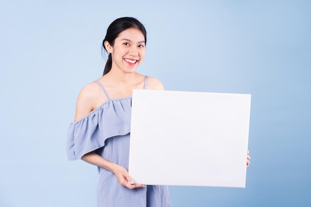 Imagem de menina asiática segurando um quadro branco, isolado em um fundo azul