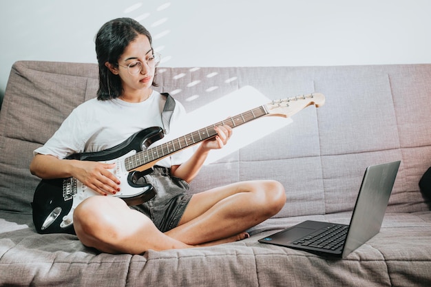 Imagem de mulher bonita feliz tocando violão e compondo uma música. copie o espaço. mulher africana aprendendo novas habilidades. assistindo a aula no laptop.