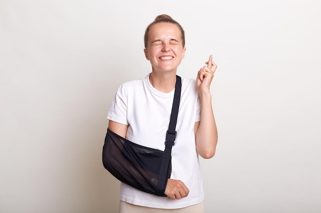 Imagem de mulher esperançosa com penteado de coque vestindo camiseta casual posando isolado sobre fundo branco tem trauma em pé com dedos cruzados espero que sua lesão não seja grave