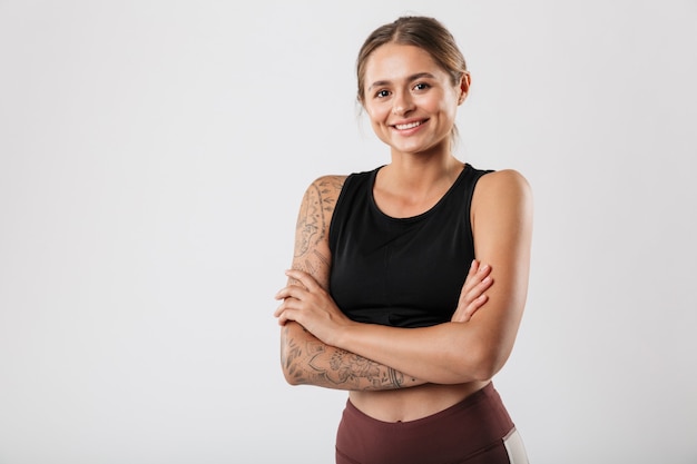 Imagem de mulher fitness em roupas esportivas sorrindo e em pé com os braços cruzados isolado sobre uma parede branca