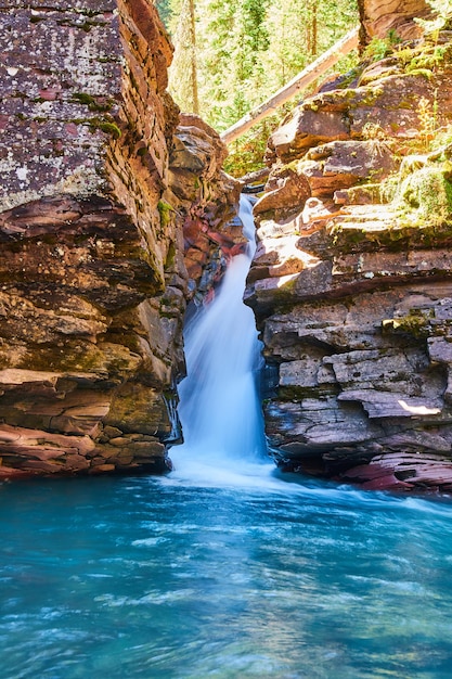 Imagem de penhascos íngremes cobertos de líquen com cachoeira e água azul