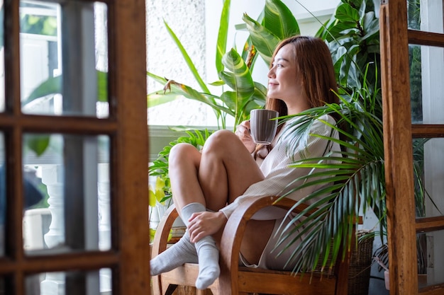 Imagem de retrato de uma linda mulher asiática bebendo café quente e relaxando na varanda com jardim de plantas em casa