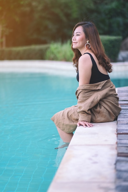 Imagem de retrato de uma linda mulher asiática gostando de sentar à beira da piscina