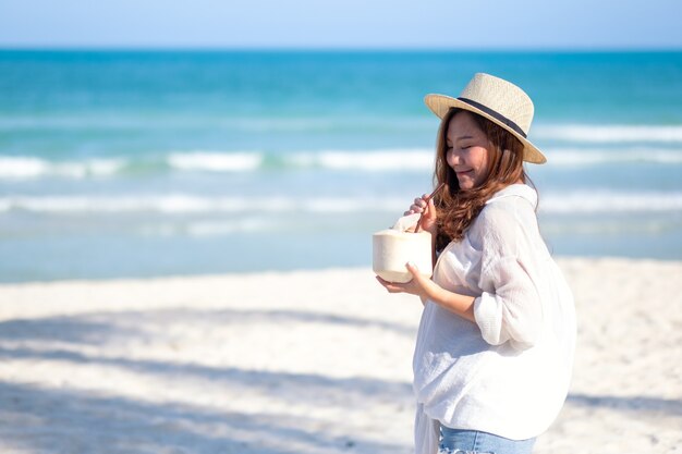 Imagem de retrato de uma linda mulher asiática segurando e bebendo suco de coco na praia