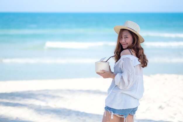 Imagem de retrato de uma linda mulher asiática segurando e bebendo suco de coco na praia