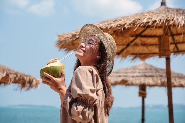 Imagem de retrato de uma linda mulher asiática segurando um coco fresco e curtindo na praia