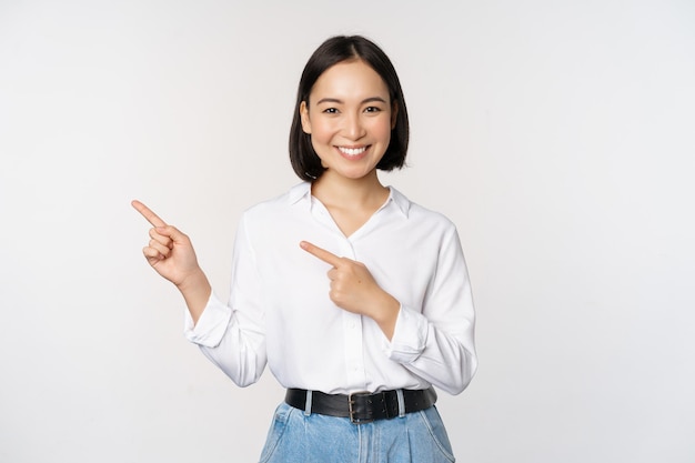 Imagem de sorridente jovem do escritório empresário asiático apontando os dedos para a esquerda mostrando o gráfico de informações do cliente do banner de lado no fundo branco do espaço de cópia
