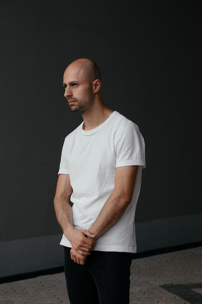 Imagem de um bonito homem careca em uma camiseta branca em um fundo cinza
