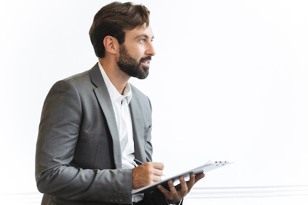 Foto imagem de um empresário barbudo confiante vestindo um terno formal olhando para a frente e fazendo anotações enquanto trabalhava no escritório