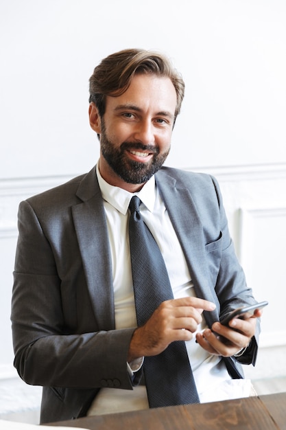 Imagem de um empresário sorridente e satisfeito usando um terno formal, digitando no celular e olhando