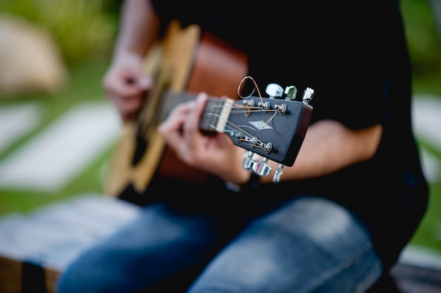 Foto imagem de um guitarrista, um jovem tocando uma guitarra enquanto está sentado em um jardim natural, conceito de música