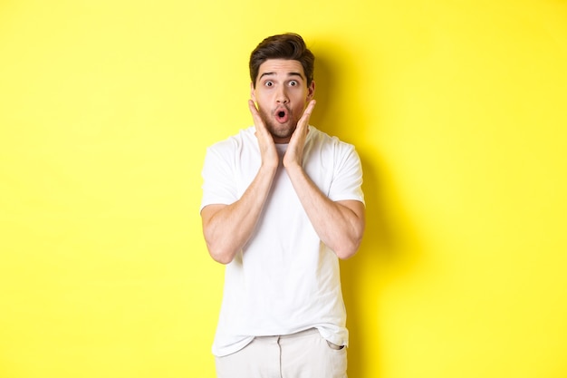 Imagem de um homem bonito parecendo surpreso, ofegando e dizendo uau, olhando para a oferta promocional surpreso, em pé sobre um fundo amarelo