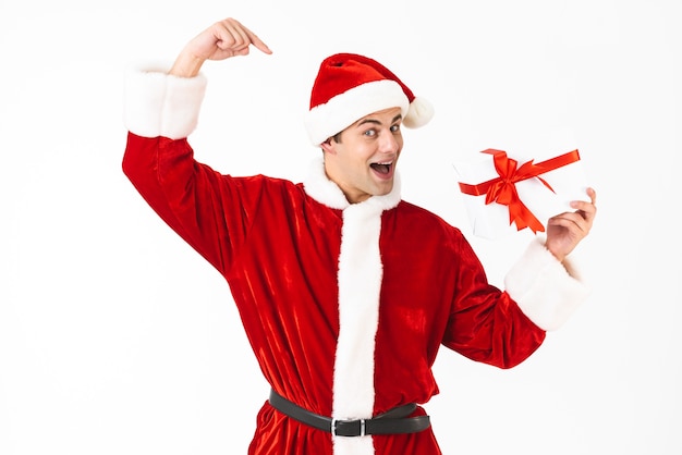 Imagem de um homem divertido, na casa dos 30 anos, com fantasia de Papai Noel e chapéu vermelho segurando uma caixa de presente