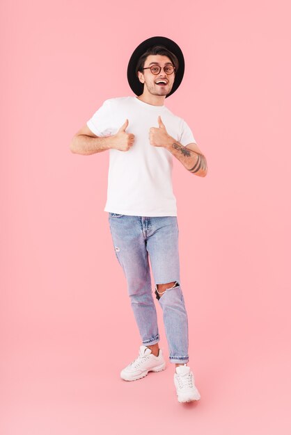 Imagem de um homem divertido usando óculos e chapéu preto apontando o polegar para cima e sorrindo