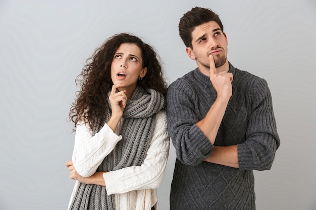 Foto imagem de um homem e uma mulher concentrados olhando para o lado enquanto pensam, isolados sobre uma parede cinza