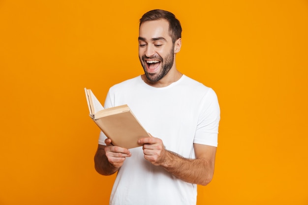 Imagem de um homem feliz de 30 anos em uma camiseta branca segurando e lendo um livro, isolado