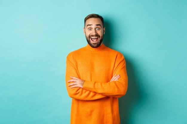 Imagem de um homem feliz e surpreso reagindo às notícias, parecendo surpreso, em um suéter laranja