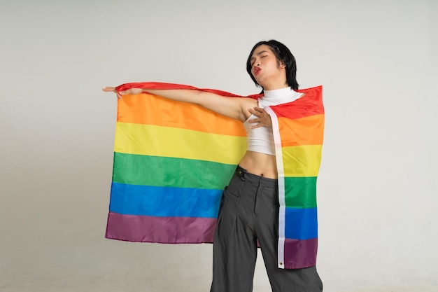 Imagem de um homem gay asiático segurando uma bandeira de arco-íris posando com confiança em um fundo branco