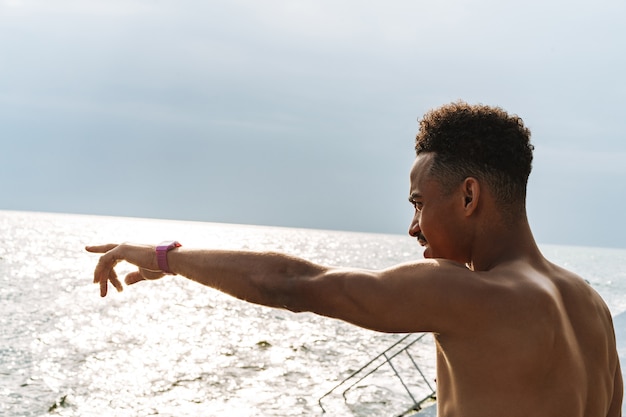 Imagem de um homem jovem e bonito esportes africanos ao ar livre no mar da praia apontando.