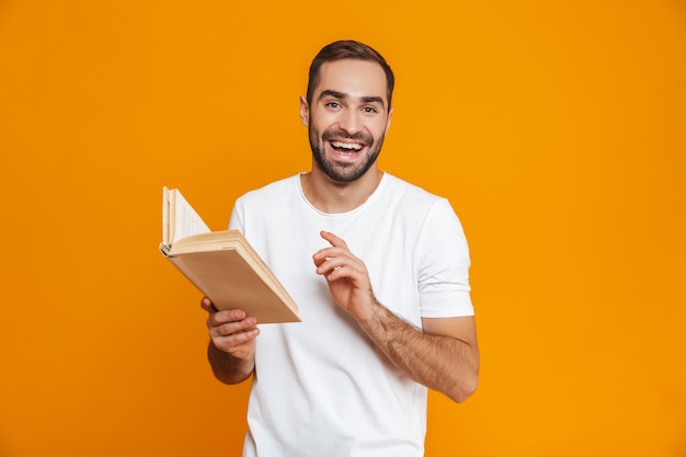 Foto imagem de um homem sorridente de 30 anos em uma camiseta branca segurando e lendo um livro, isolado