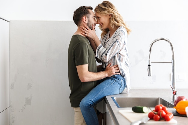 Imagem de um jovem casal amoroso feliz posando na cozinha em casa, cozinhando, abraçando e beijando.