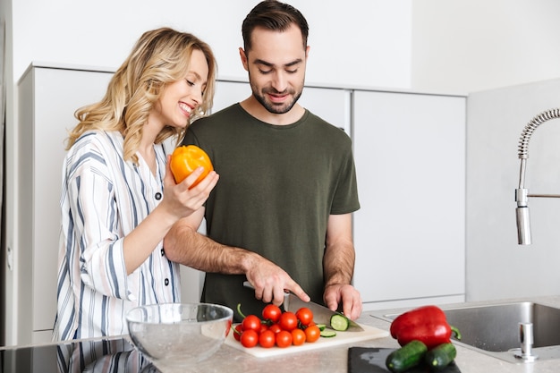 Imagem de um jovem casal amoroso feliz posando na cozinha em casa cozinhando um café da manhã.