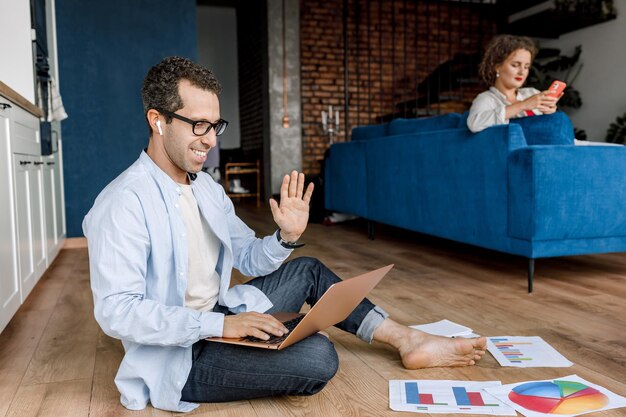 Imagem de um jovem casal de sucesso acenando para seus colegas trabalhando juntos em laptops