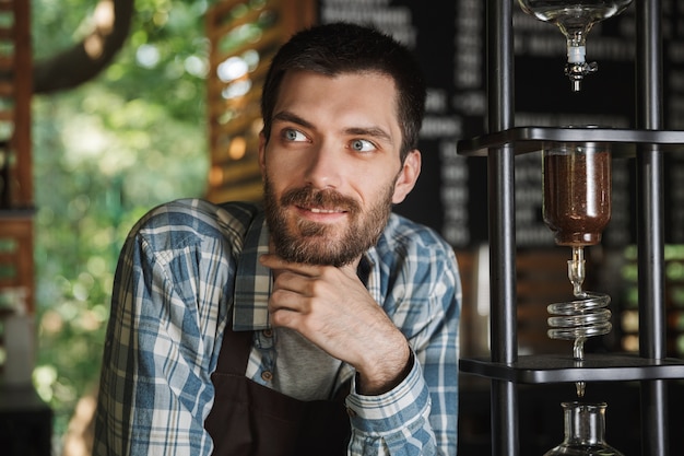 Imagem de um menino barista animado usando avental, fazendo café enquanto trabalhava em um café ou cafeteria ao ar livre