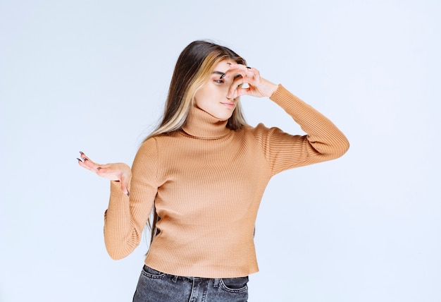 Imagem de um modelo de jovem com suéter marrom em pé e cobrindo o nariz.