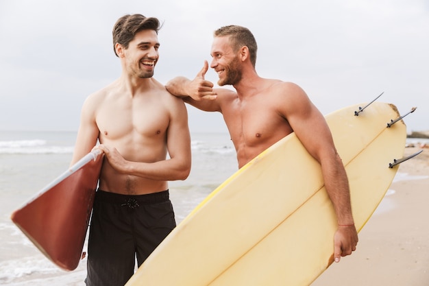 Imagem de um sorridente amigo de surfistas de dois homens com surfistas em uma praia do lado de fora conversando um com o outro.