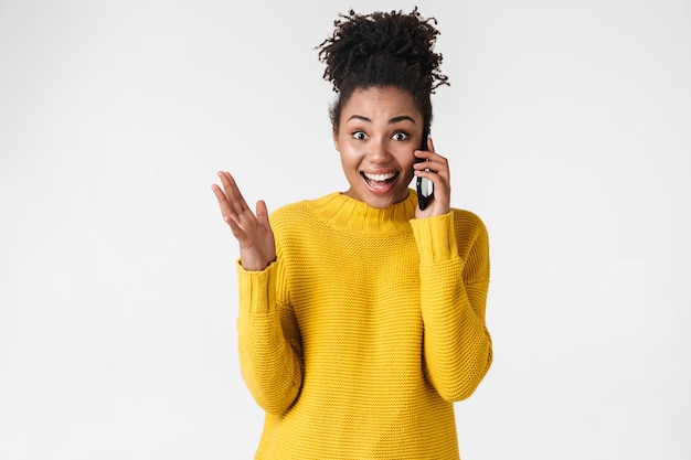 Imagem de uma bela jovem africana animado emocional feliz mulher posando sobre uma parede branca, falando por telefone celular.