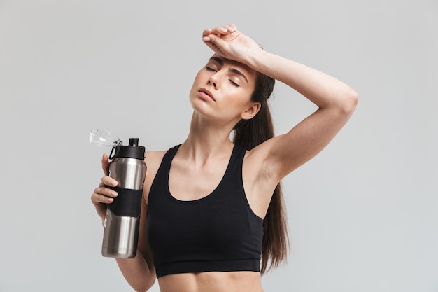 Imagem de uma bela jovem esporte fitness mulher bebendo água isolada sobre uma parede cinza.
