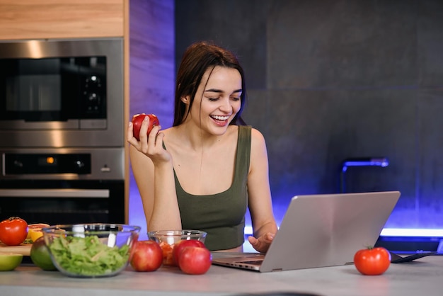 Imagem de uma bela jovem estudante com maçã sentada dentro de casa usando um computador portátil