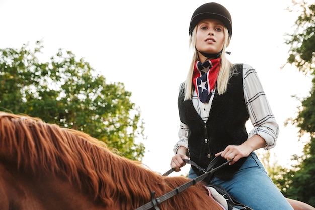 Imagem de uma bela jovem loira com chapéu, cavalgando no quintal no campo