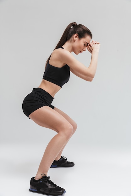 Imagem de uma bela jovem mulher de fitness esporte fazer exercícios isolados sobre uma parede cinza.
