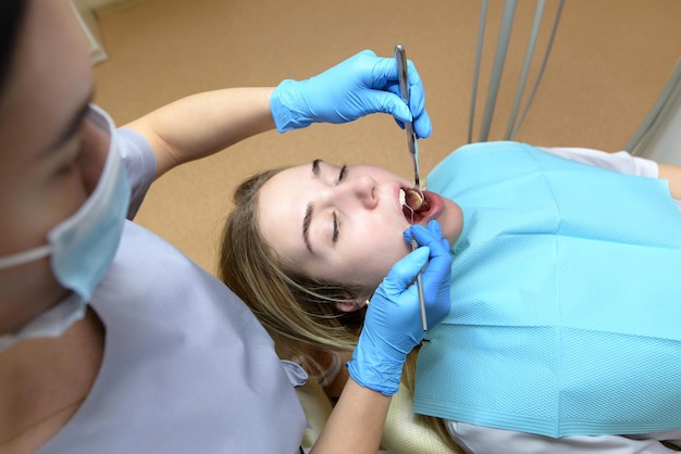 Imagem de uma bela jovem sentada em uma cadeira odontológica em um centro médico enquanto um médico profissional conserta seus dentes