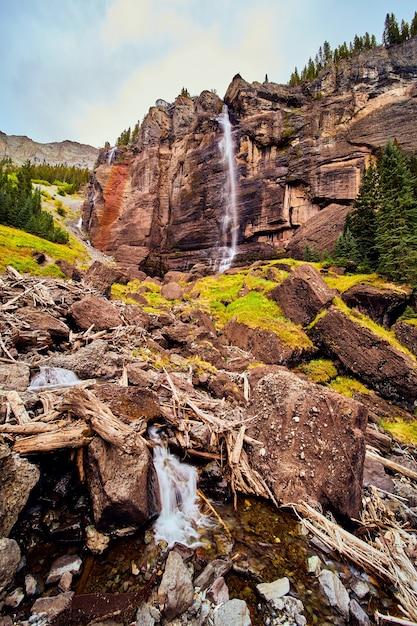 Imagem de uma cachoeira gigantesca sobre penhascos verticais levando a pedras de musgo no vale