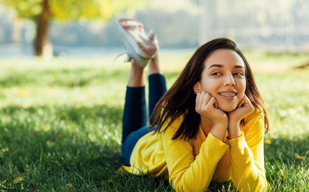Imagem de uma jovem adolescente feliz sorrindo e relaxando do lado de fora no parque verde da natureza Linda jovem alegre deitada ao ar livre na grama verde no parque da cidade
