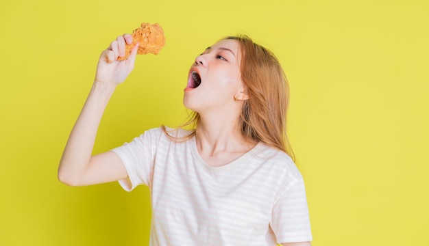 Imagem de uma jovem asiática comendo frango frito em fundo amarelo